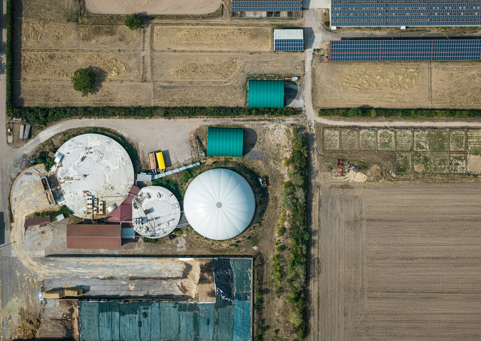 Aerial view of a biogas plant with circular tanks and fields.