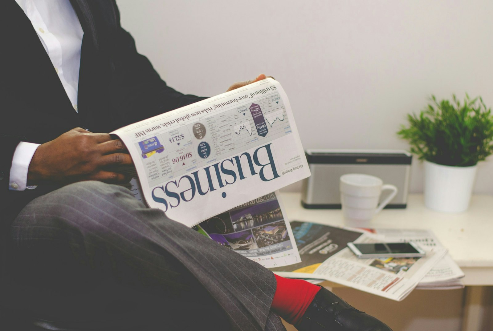 Person sitting near table holding newspaper.