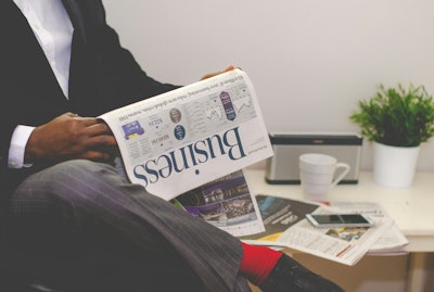 Person sitting near table holding newspaper.