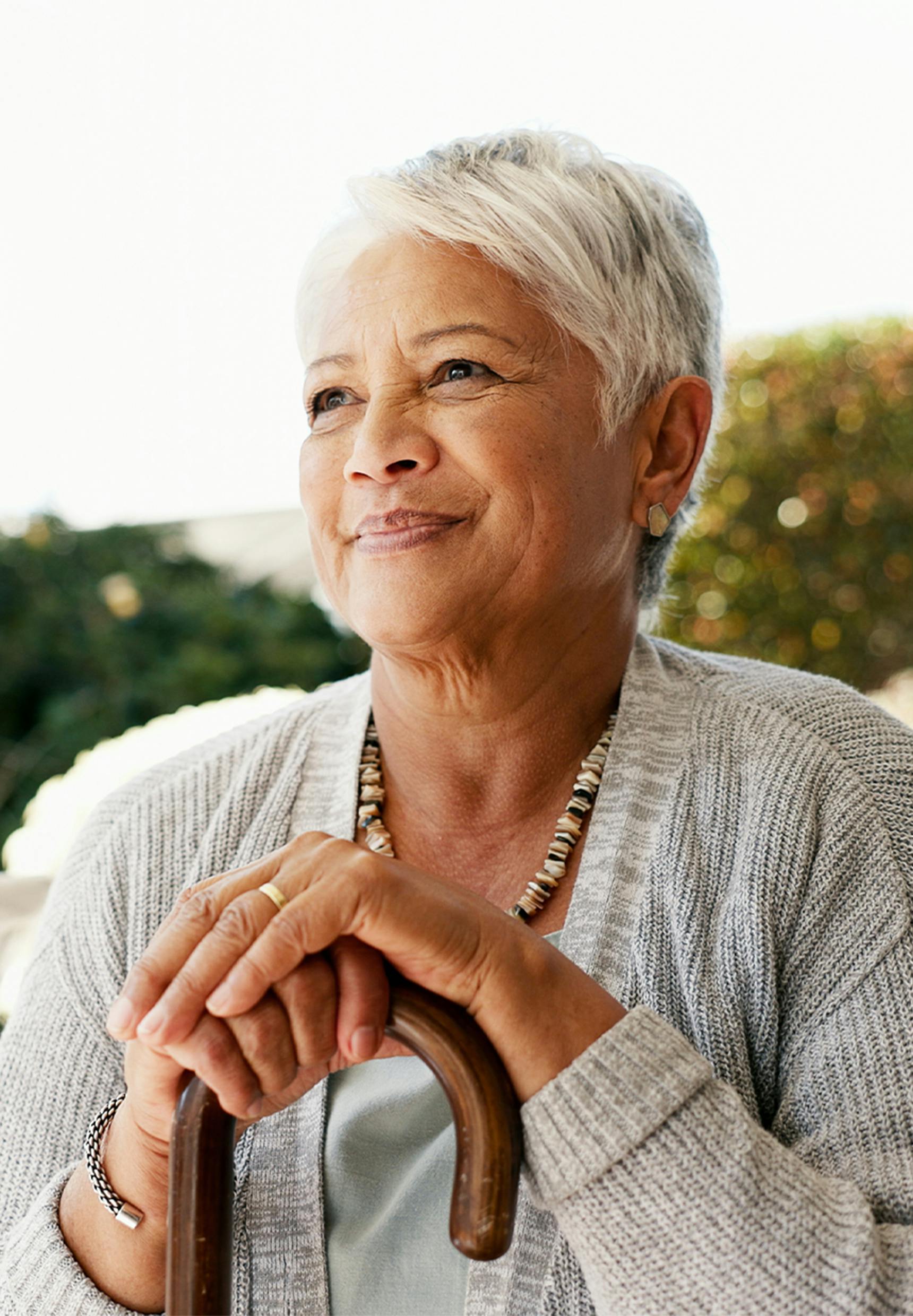 older woman smiling, resting her hands on her cane