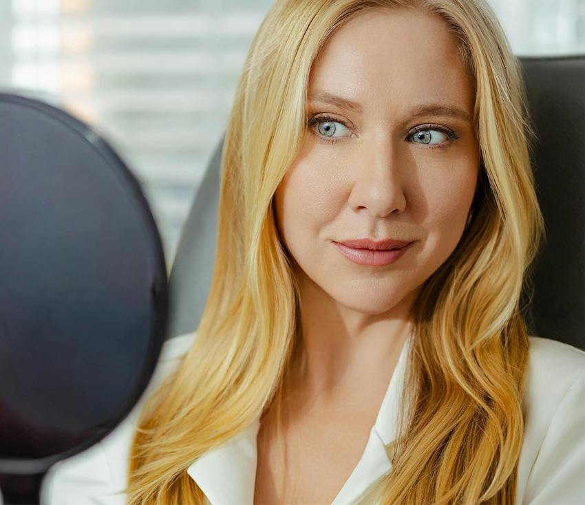 Blonde woman with blue eyes in white blazer, professional setting