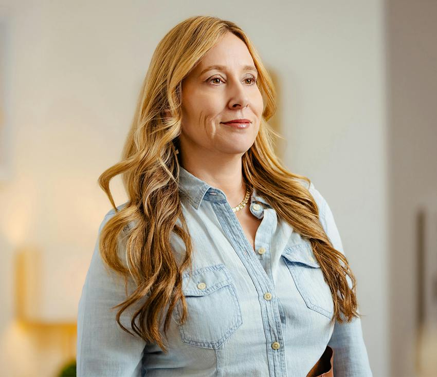 Woman with long blonde hair wearing a light blue denim shirt.