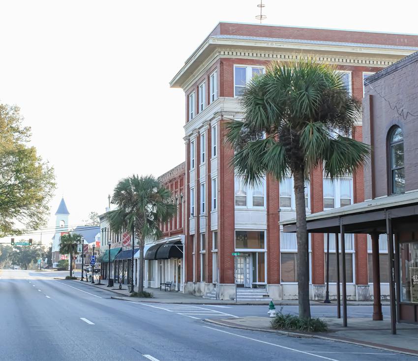 Historic brick downtown streetscape in Waycross, Georgia, with palm trees lining the road.