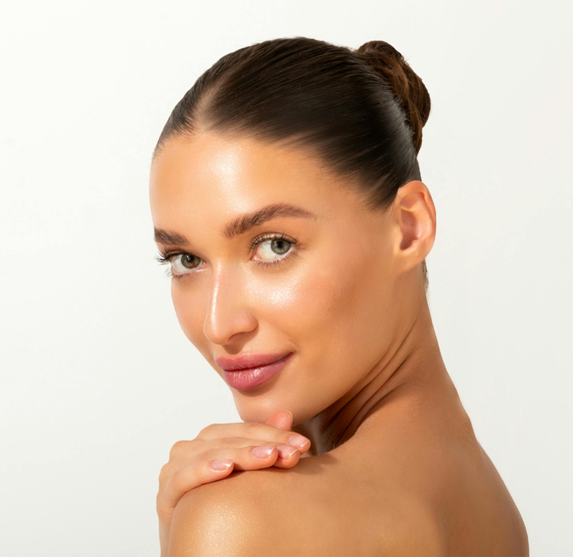 Woman with glowing skin and hair in bun, looking over shoulder