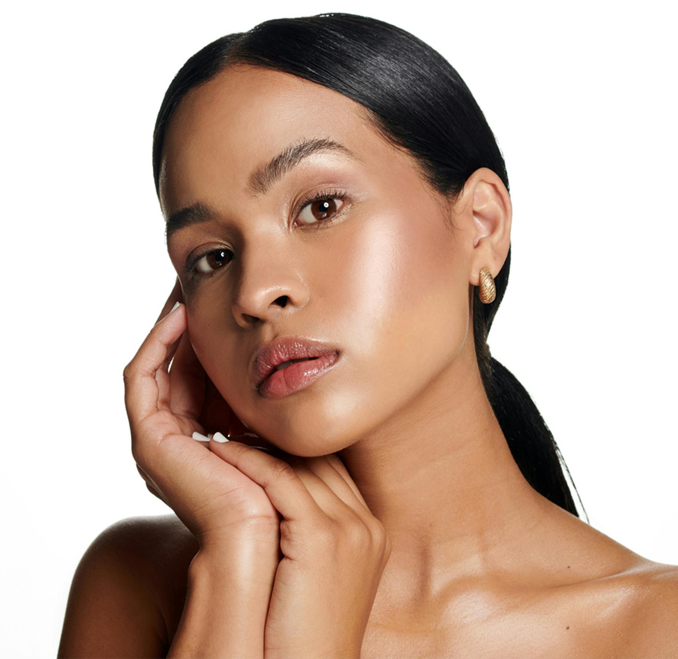 Woman with glowing skin, sleek hair, and gold hoop earrings posing.
