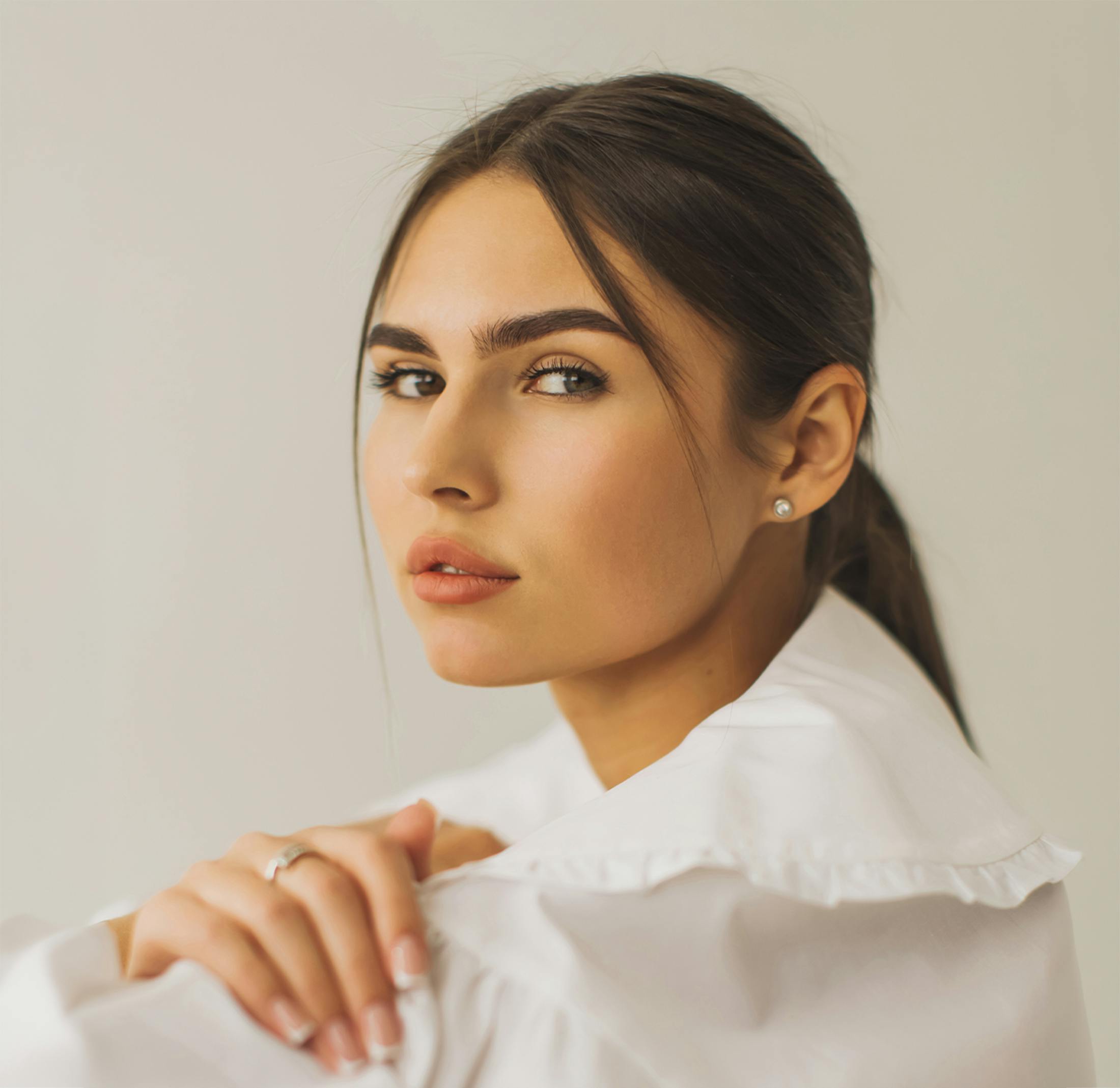 Young woman with defined nose profile, wearing white blouse and pearl earring.