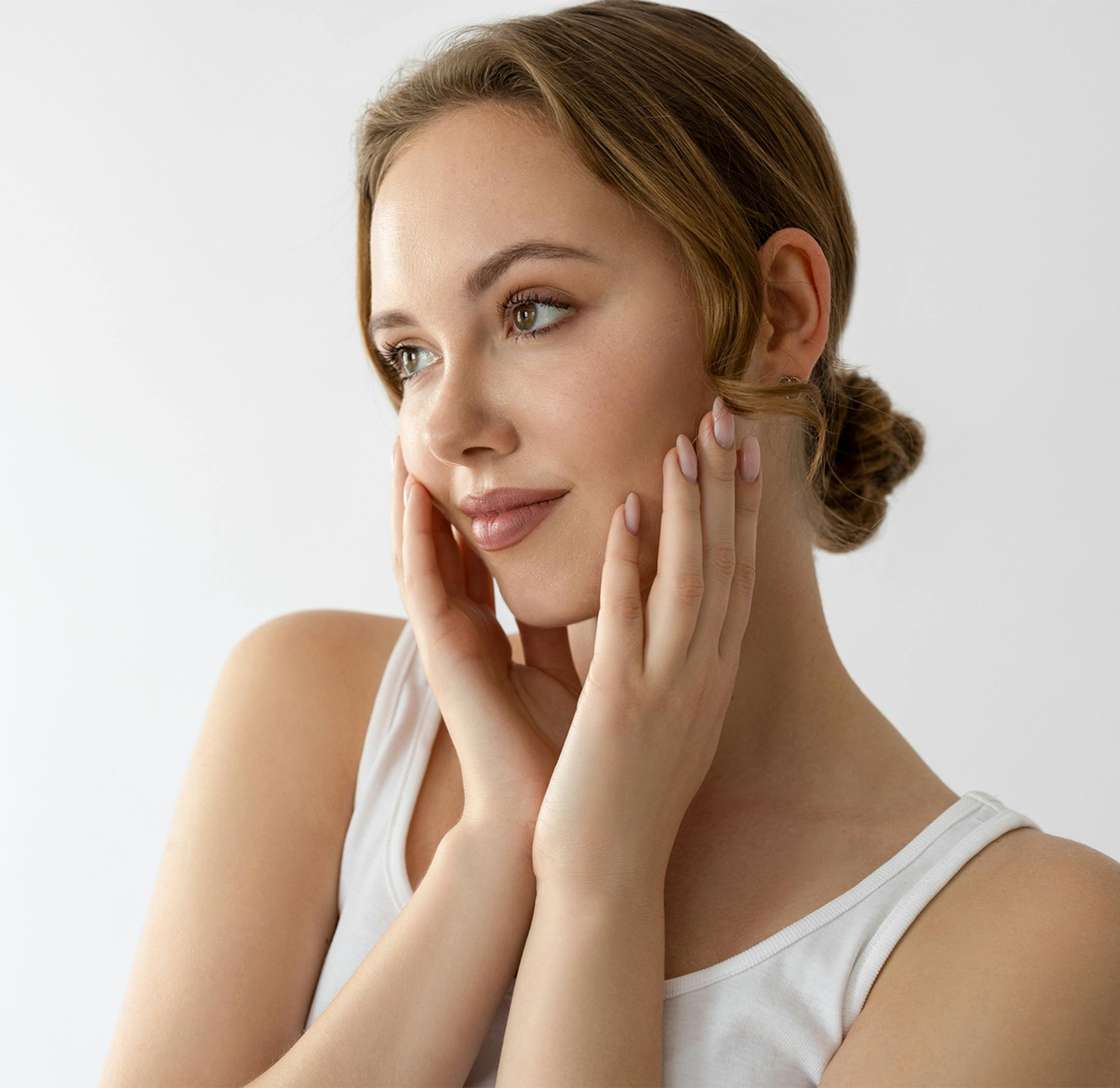 Young woman with clear skin gently touching her face with both hands.