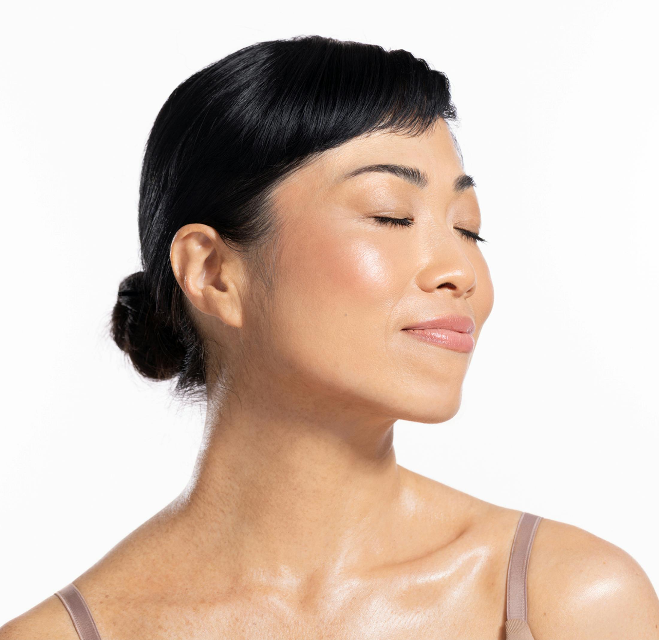 Woman with glowing skin and closed eyes, hair in a bun