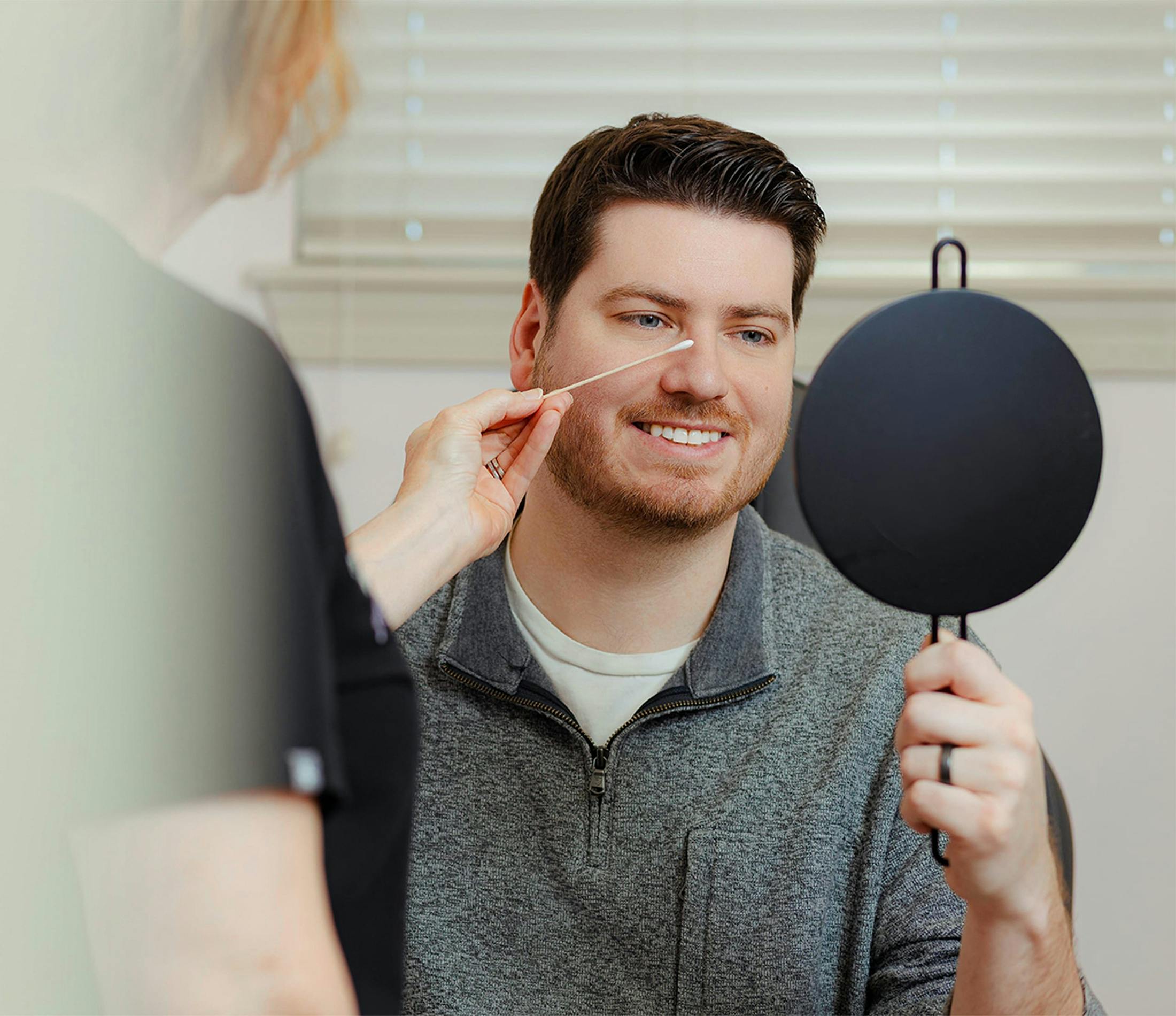 man looking at his reflection in a handheld mirror