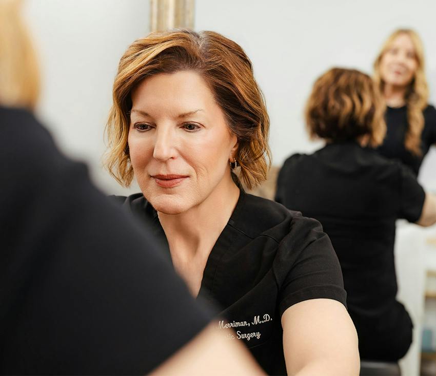 Dr. Merriman, M.D., plastic surgeon in black scrubs consulting a patient