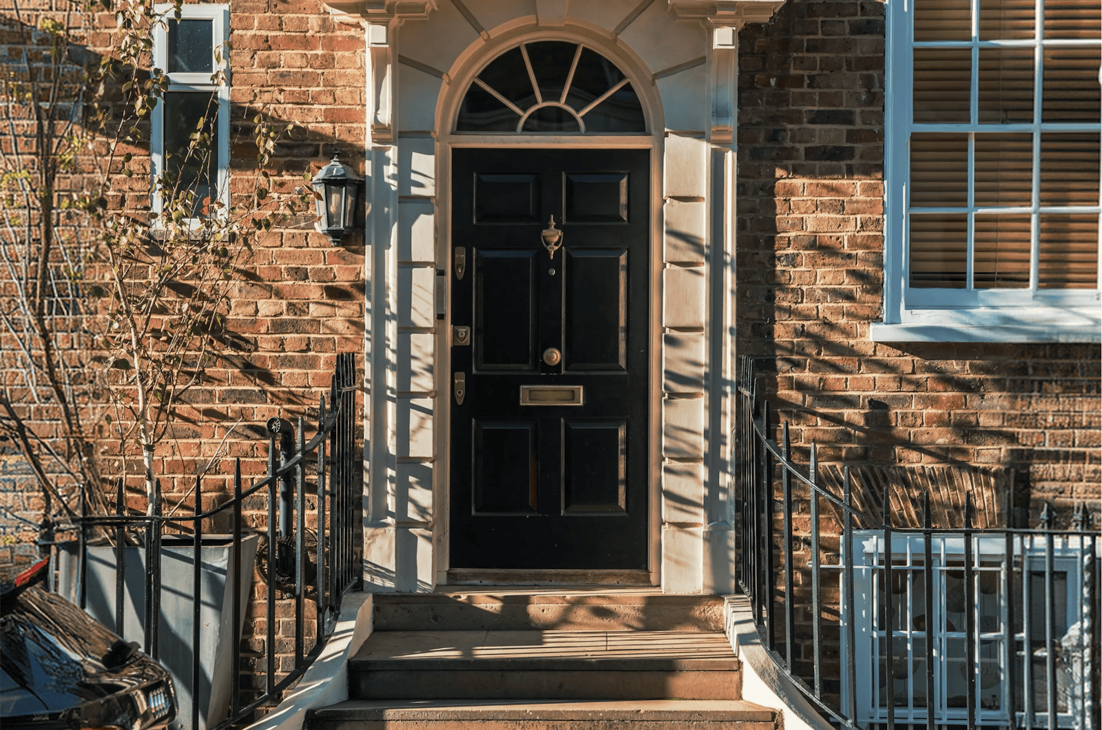 A dark brown door in a red brick house with white window frames.