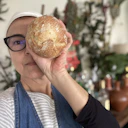 Chef Graziela Scorvo Tavares de frente para a câmera, segurando o pão em frente ao rosto