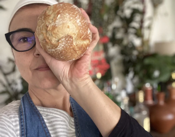 Chef Graziela Scorvo Tavares de frente para a câmera, segurando o pão em frente ao rosto