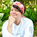 Chef Leticia Massula, aparece de frente com um lenço vermelho na cabeça.