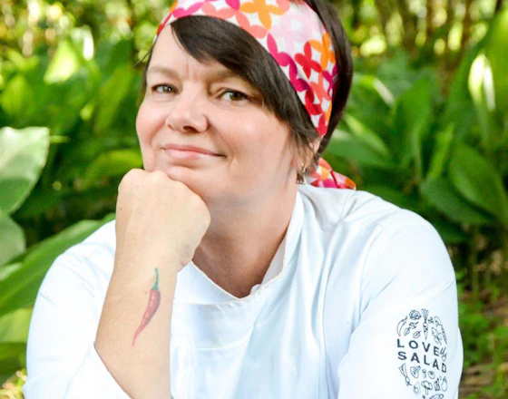 Chef Leticia Massula, aparece de frente com um lenço vermelho na cabeça.