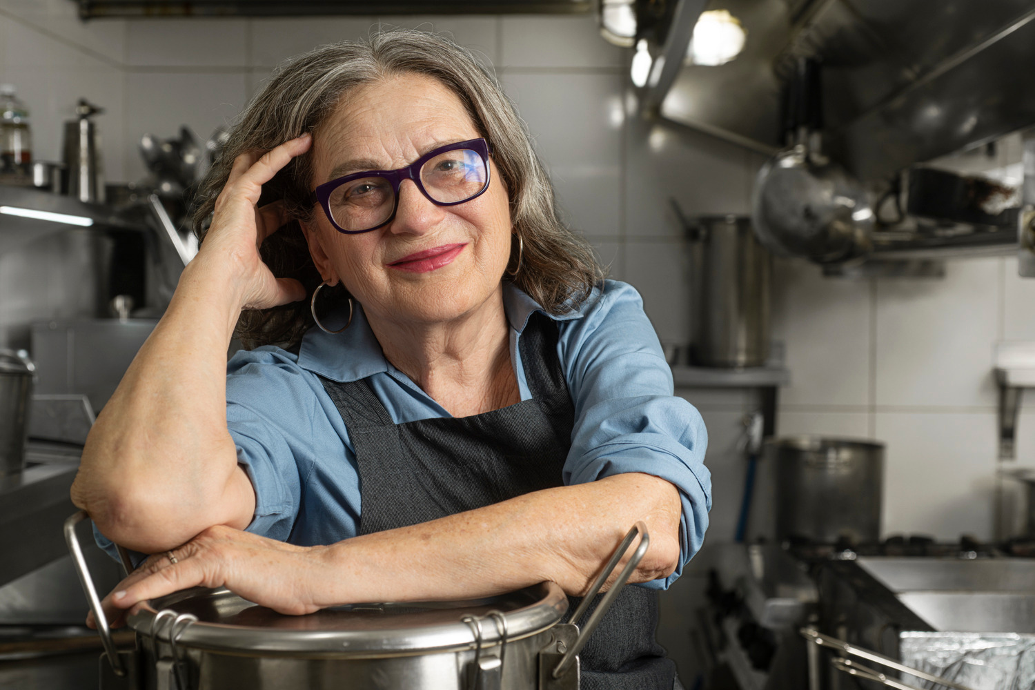 Chef Mara Salles, numa cozinha, posando apoiada em uma panela.