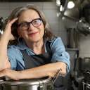 Chef Mara Salles, numa cozinha, posando apoiada em uma panela.