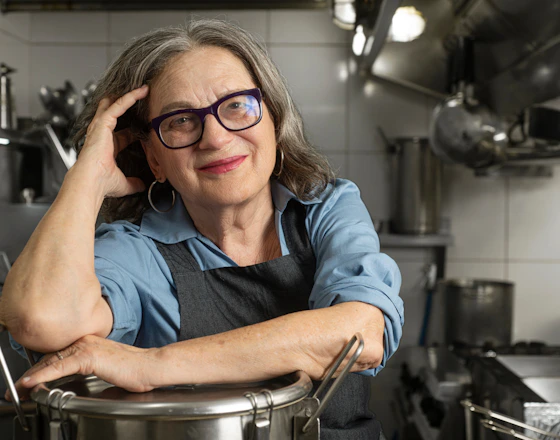 Chef Mara Salles, numa cozinha, posando apoiada em uma panela.