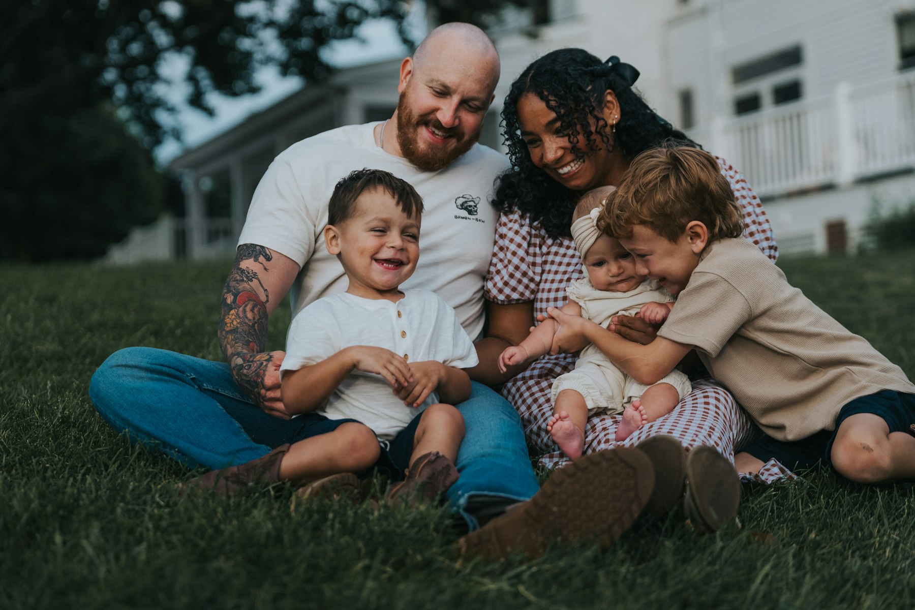 Family of five sitting together in the grass and laughing at Veterans Memorial Park in Avon Lake, Ohio