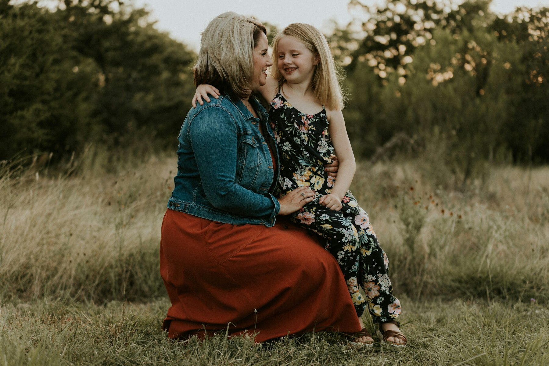 Mom holding her daughter on her lap in a field during a golden hour family session