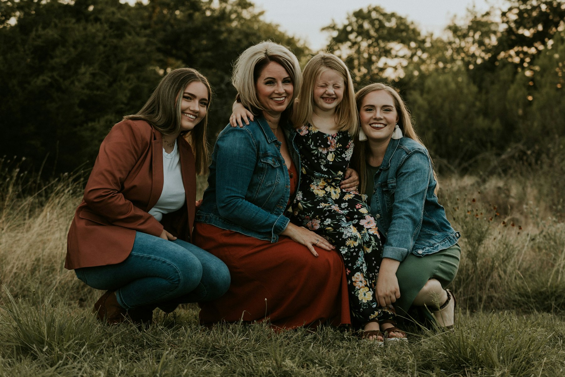 Mom and three daughters kneeling in the grass and laughing during a golden hour family session