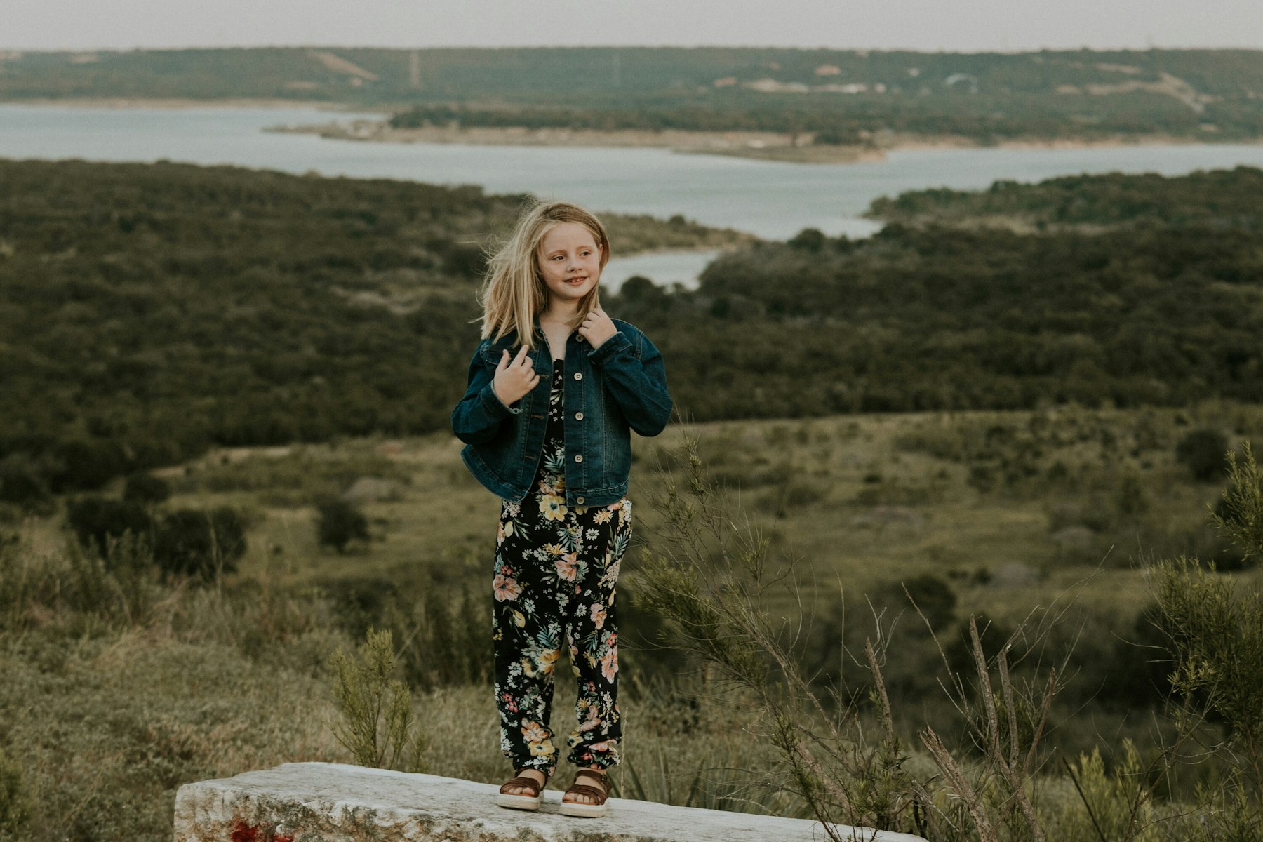 Girl standing on a stone wall above the lake, wide landscape during a golden hour family session