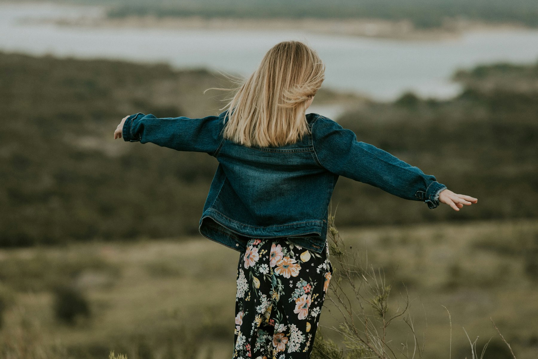 Girl in a denim jacket with arms out over the valley during a golden hour family session