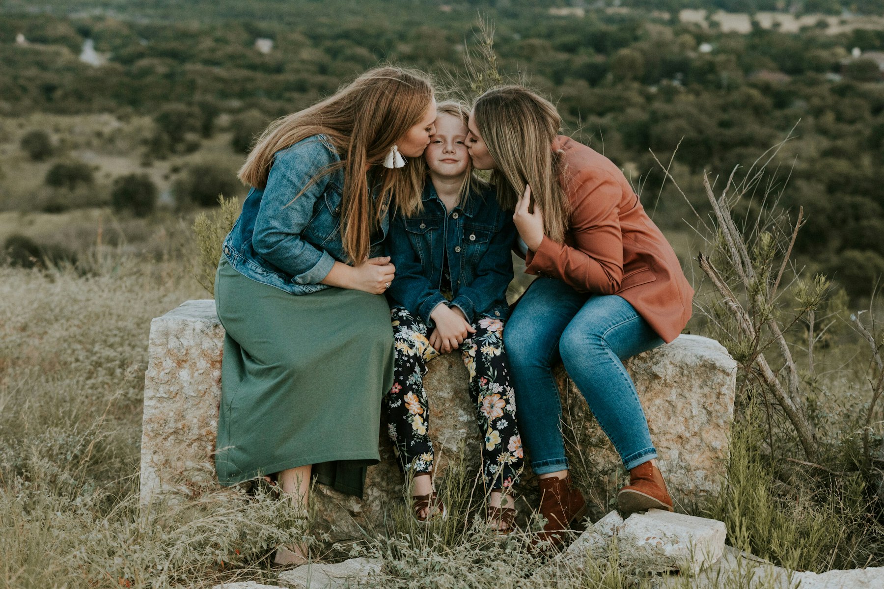 Mom hugging her daughters on a rock ledge during a golden hour family session