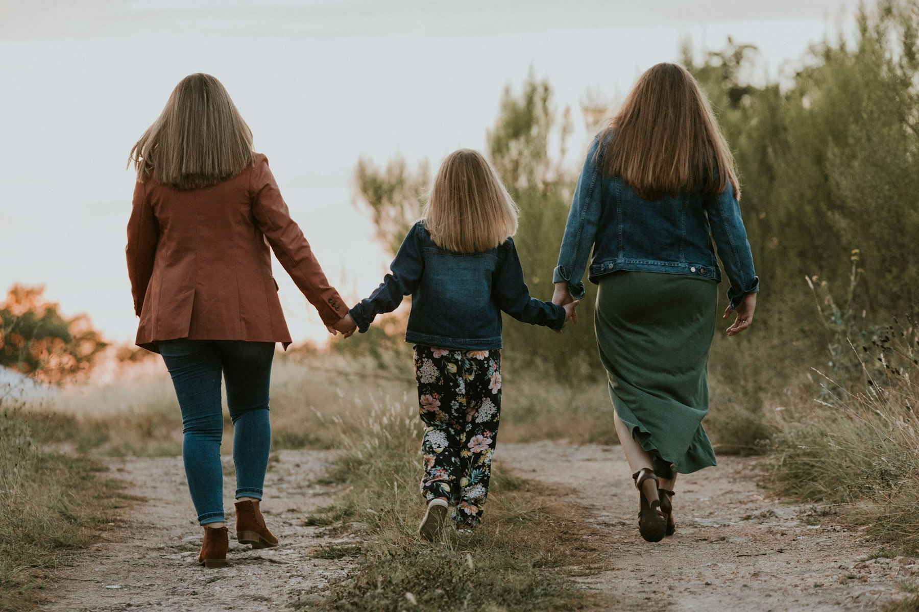 Mom and daughters walking a dirt path at sunset holding hands during a golden hour family session