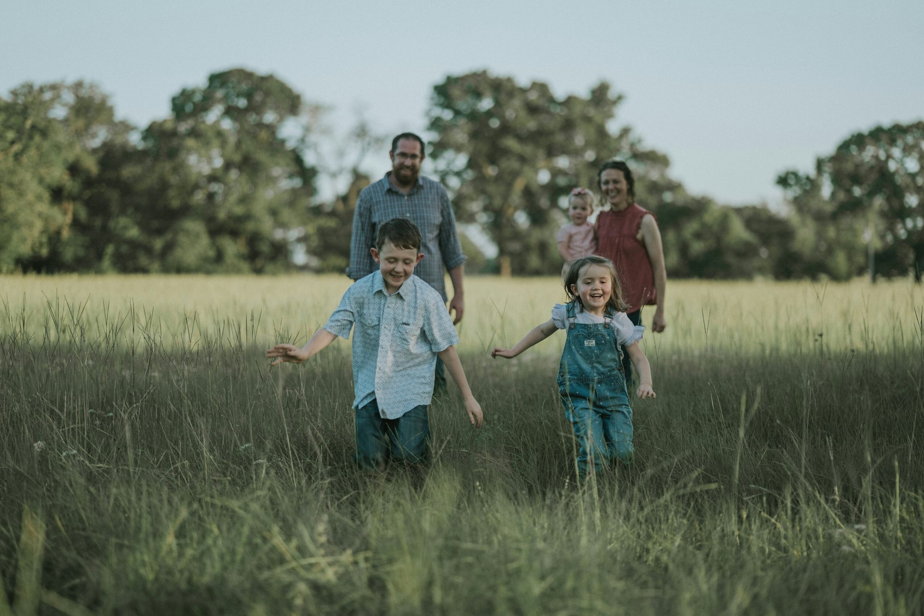 Family walking hand in hand across a summer field during a summer family session in a meadow