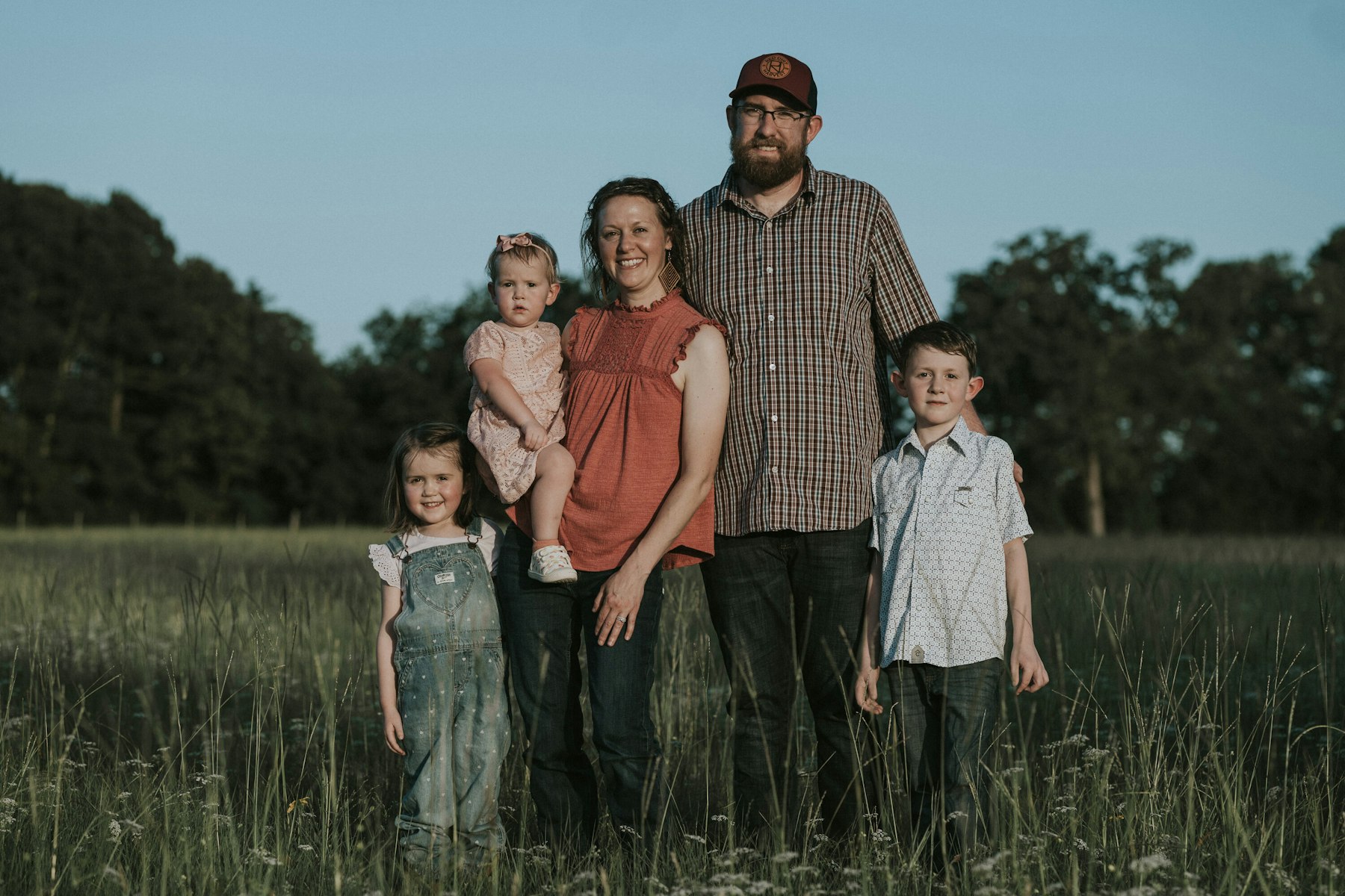 Family of five standing in the field, mom holding the baby during a summer family session in a meadow