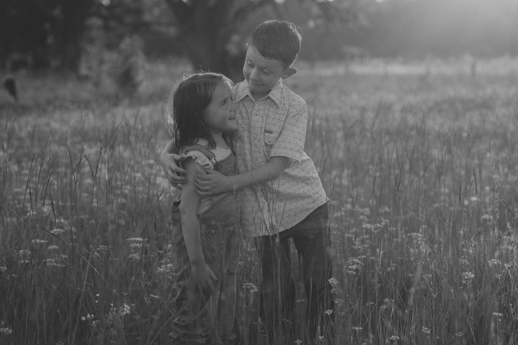 Black and white photo of a brother and sister hugging in wildflowers during a summer family session in a meadow