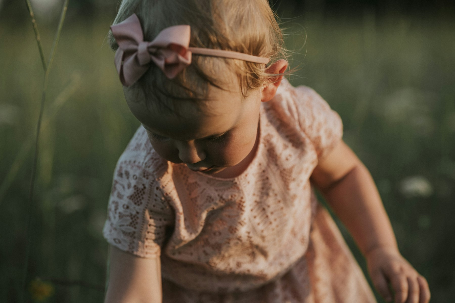 Baby girl with a pink bow, close up during a summer family session in a meadow