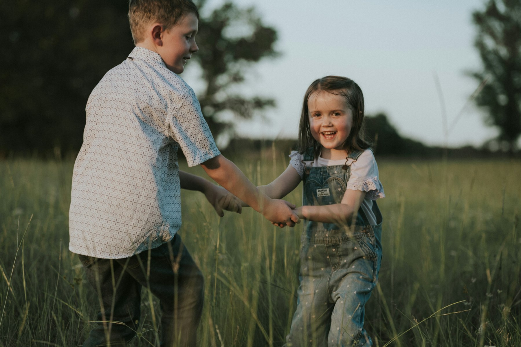 Brother and sister playing in the grass during a summer family session in a meadow