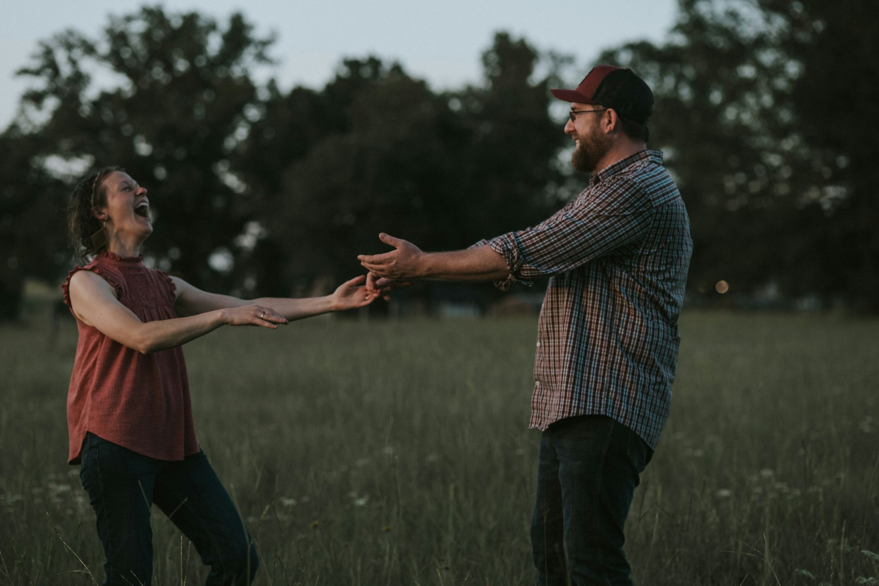 Parents laughing and reaching for each other's hands during a summer family session in a meadow
