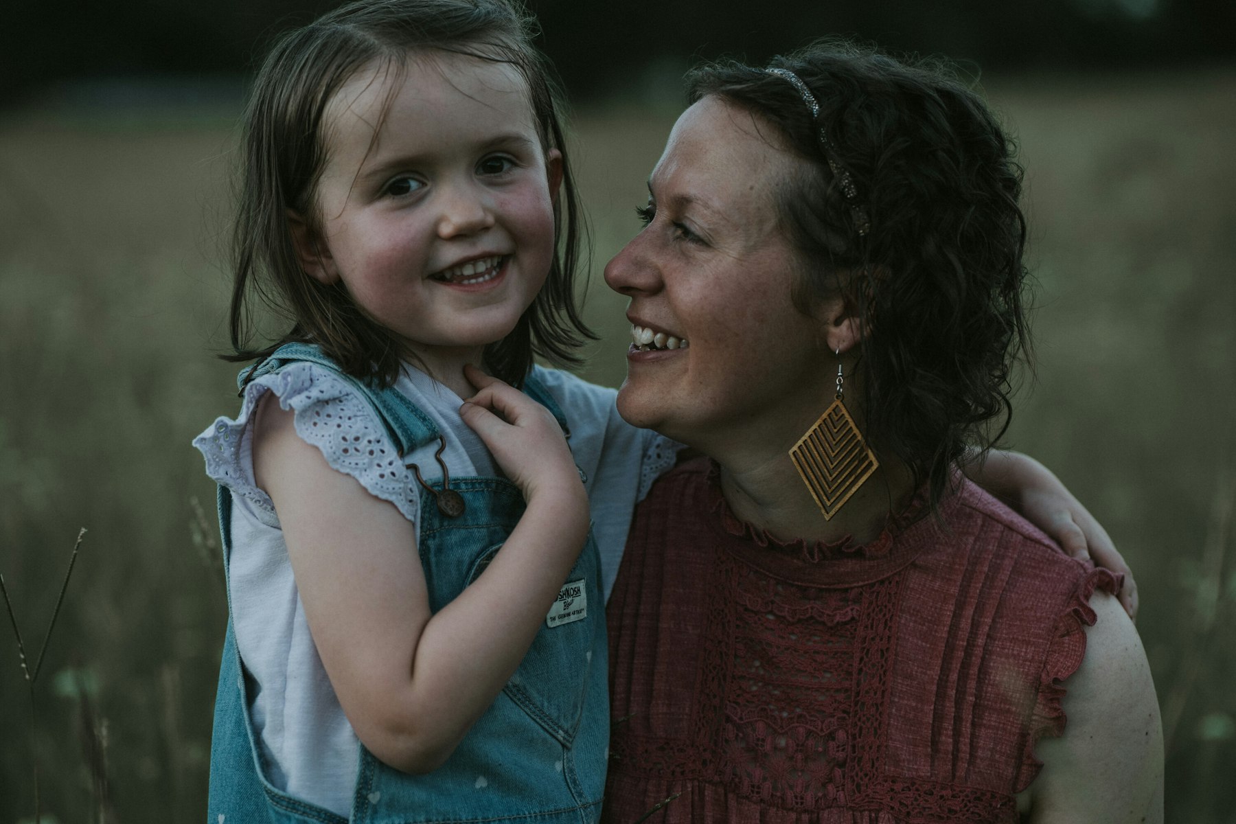 Mom hugging her daughter, both smiling during a summer family session in a meadow