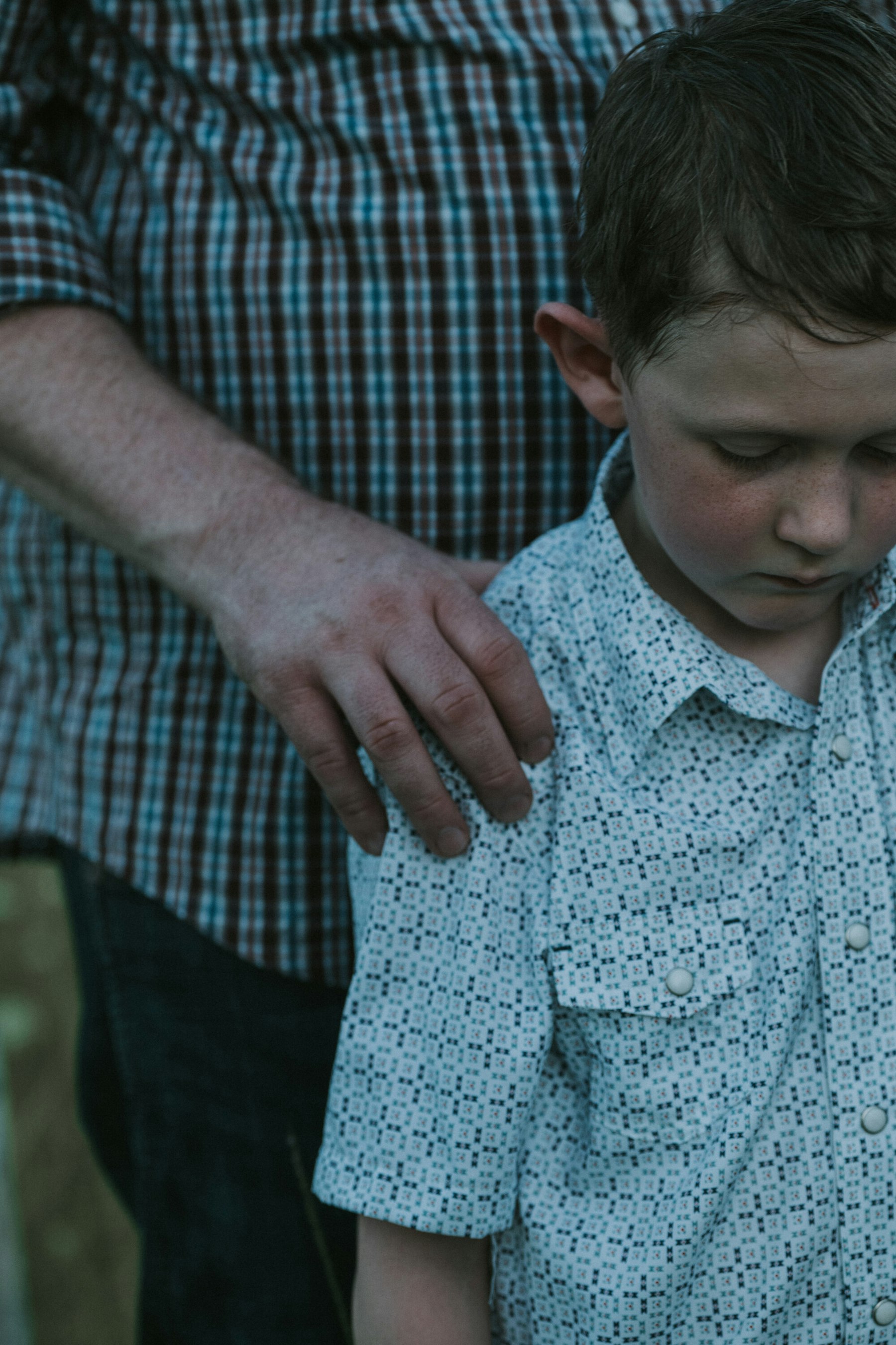 Dad's hand resting on his son's shoulder, close up during a summer family session in a meadow