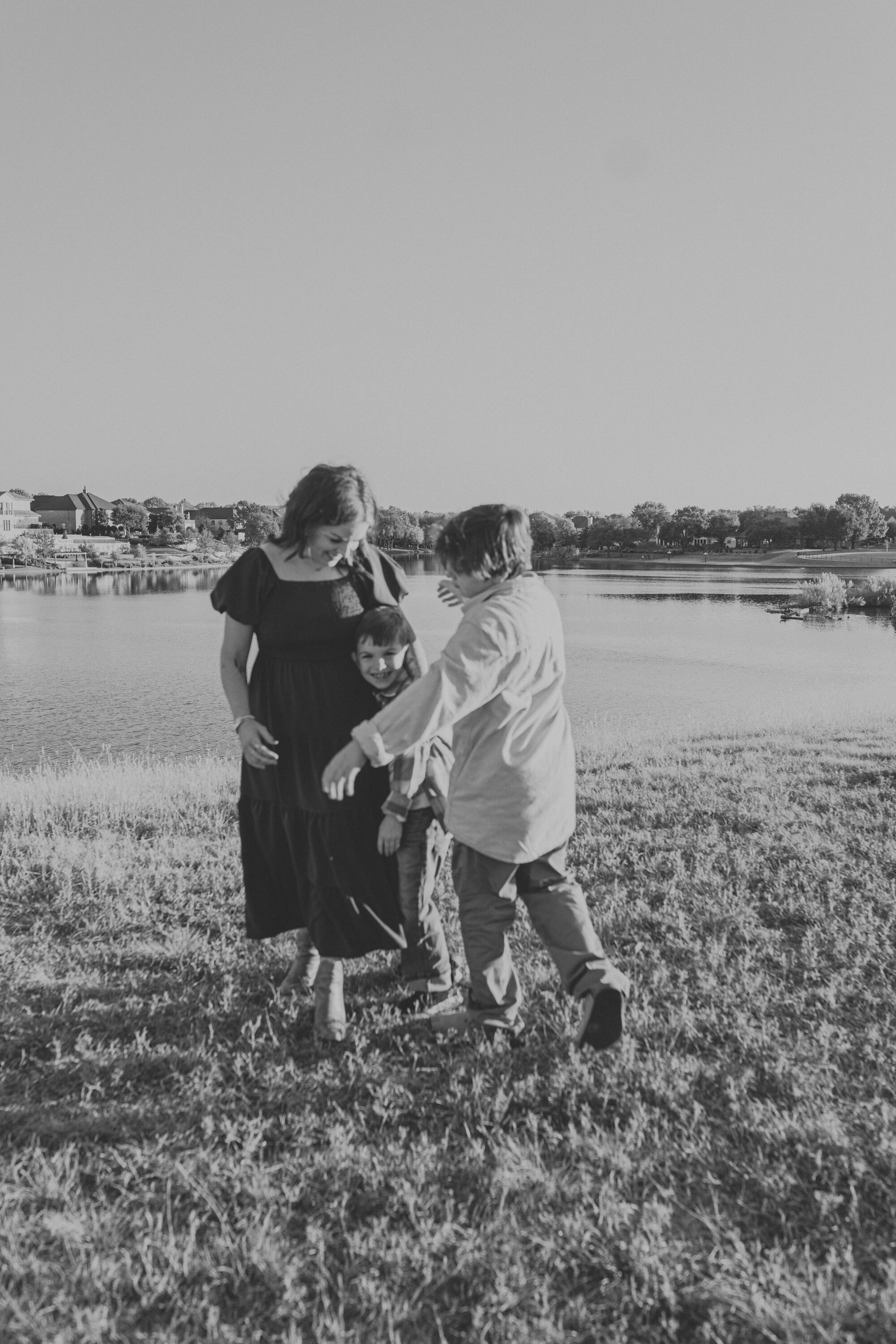 Black and white photo of a mom and her boys playing at the water's edge during a lakeside family session
