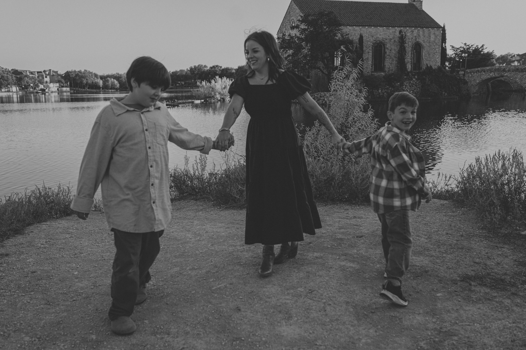 Black and white photo of a mom and sons walking hand in hand along the shore during a lakeside family session