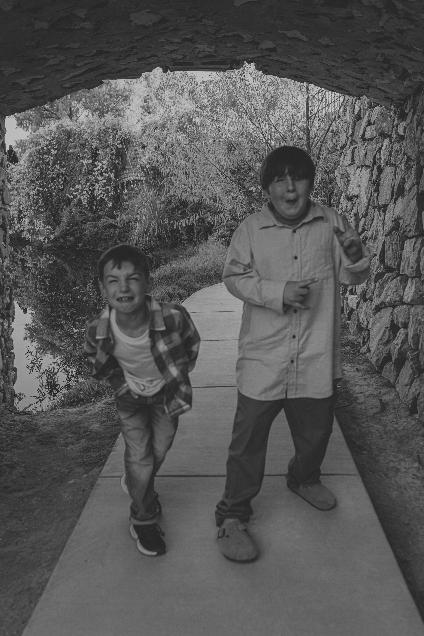 Black and white photo of two boys running through a tunnel toward the camera during a lakeside family session