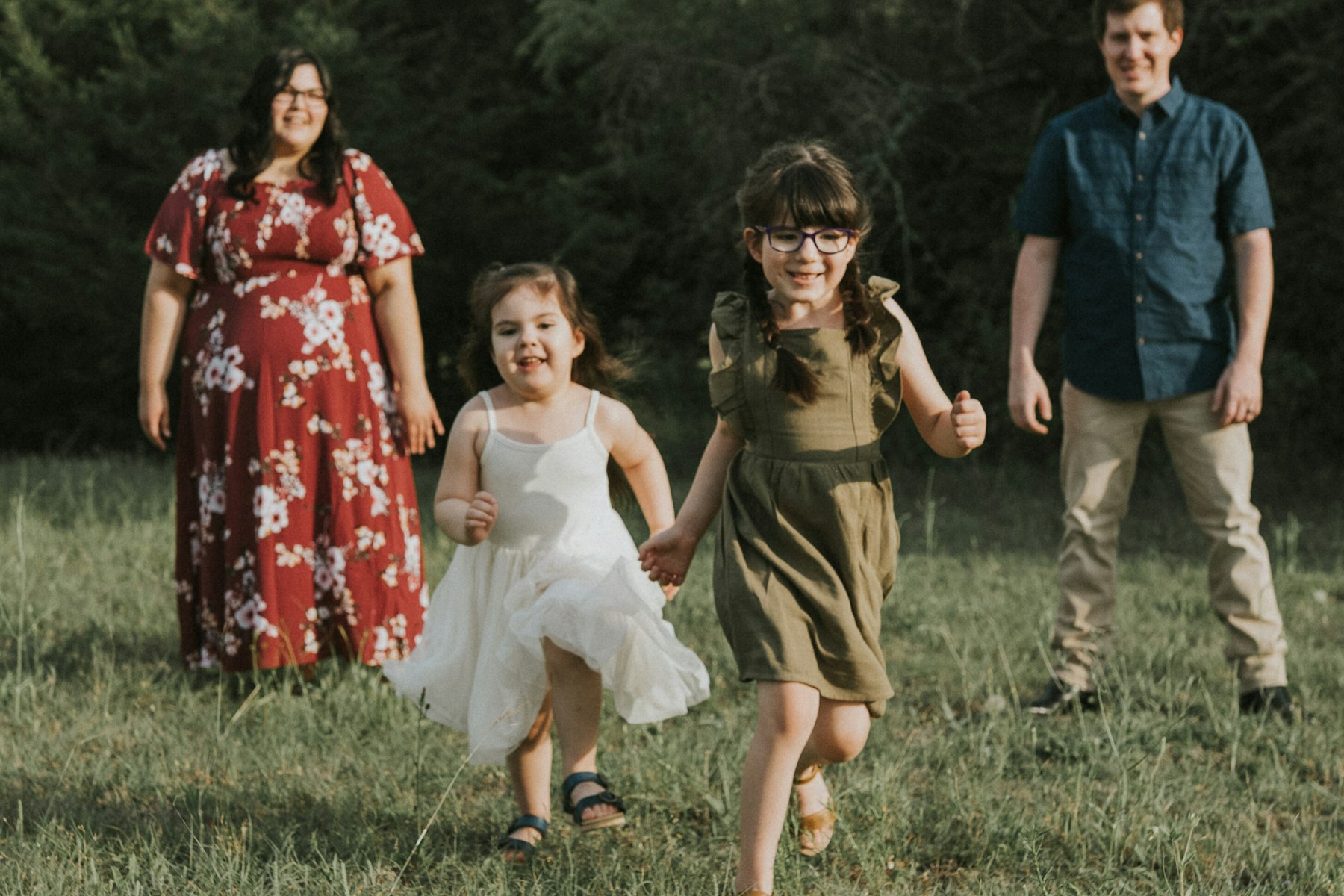 Family of four walking through the field, girls laughing during a family session