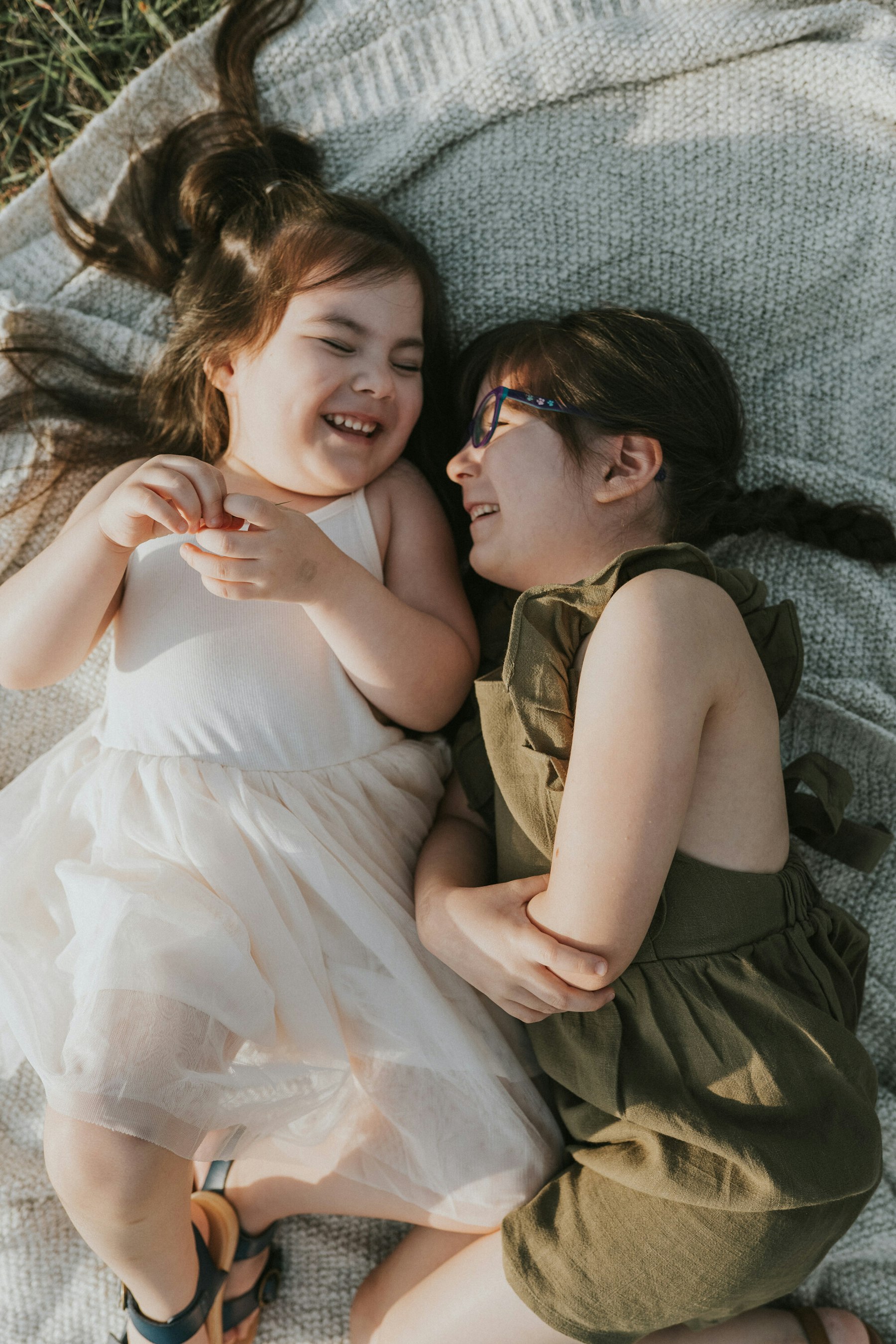 Two sisters lying on a blanket and giggling during a family session