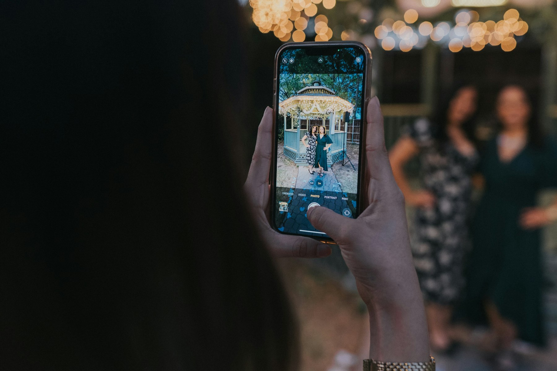 Guest photographing the reception under string lights at a garden wedding