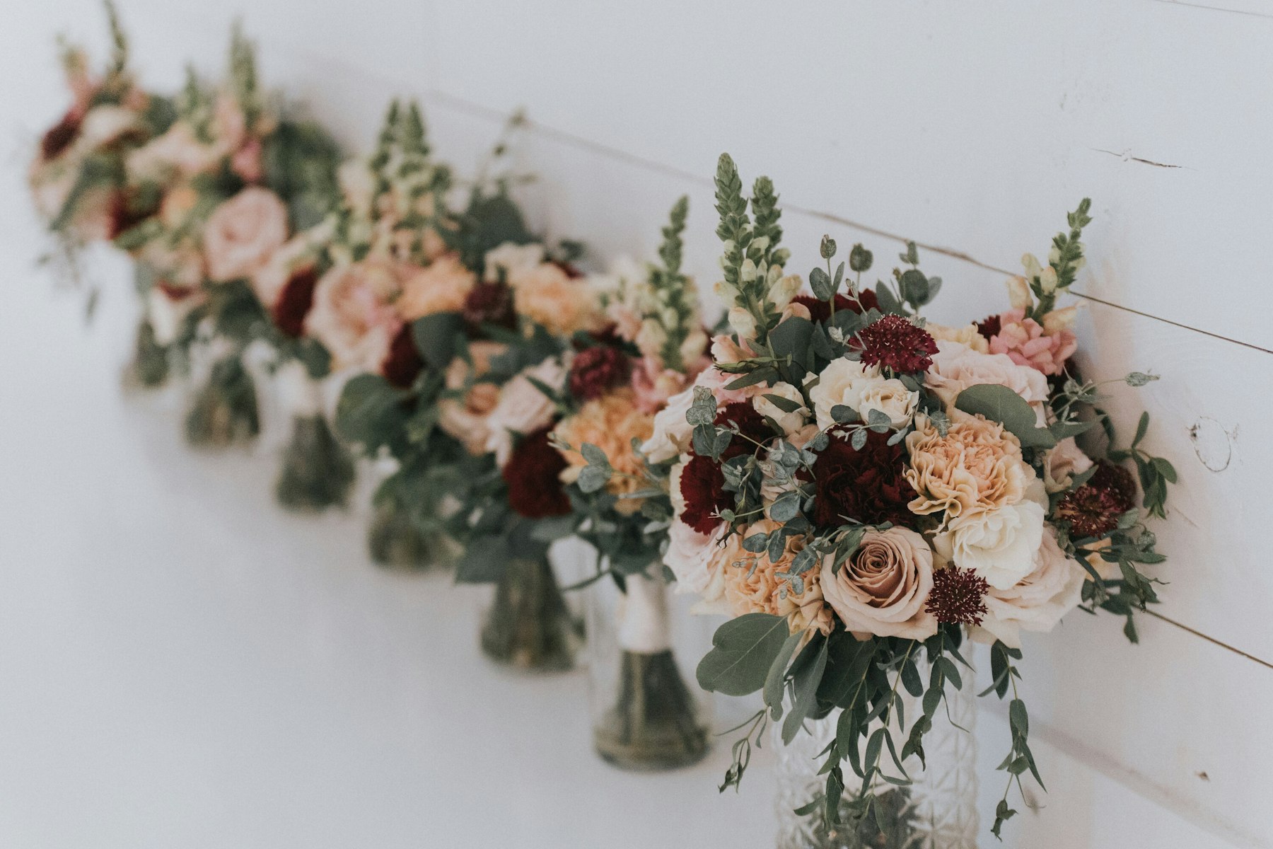 Wall mounted floral arrangement in burgundy and blush at a white barn wedding