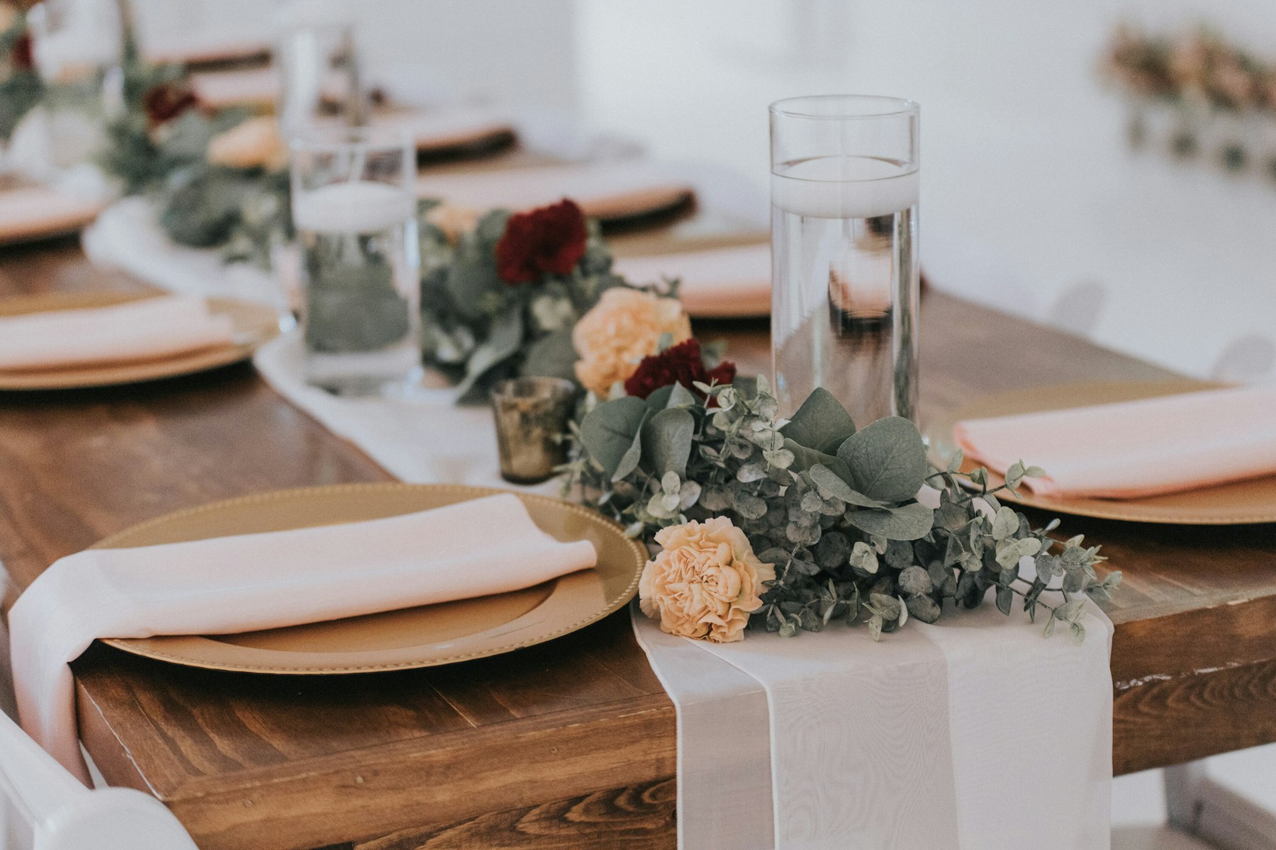 Farmhouse reception table with gold chargers and greenery at a white barn wedding