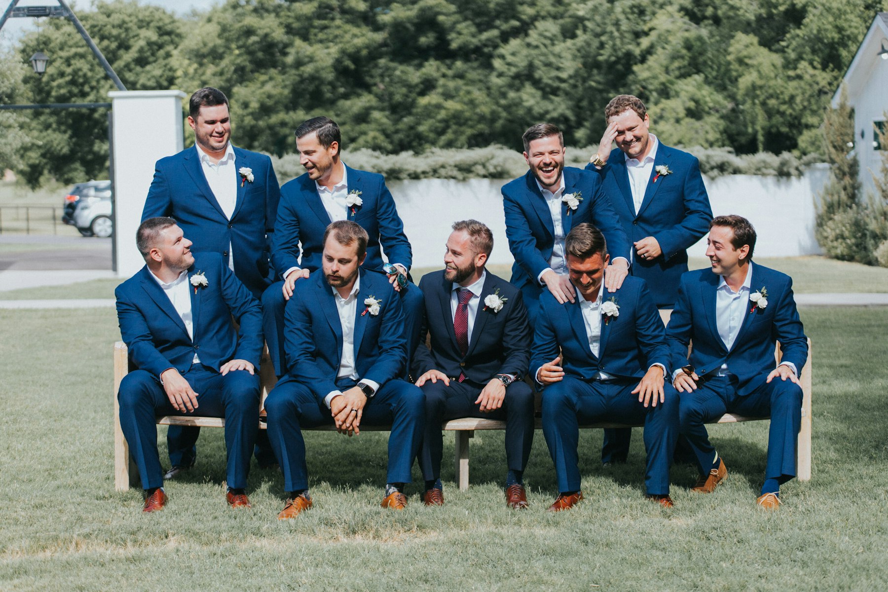 Groomsmen in navy suits laughing on a bench at a white barn wedding
