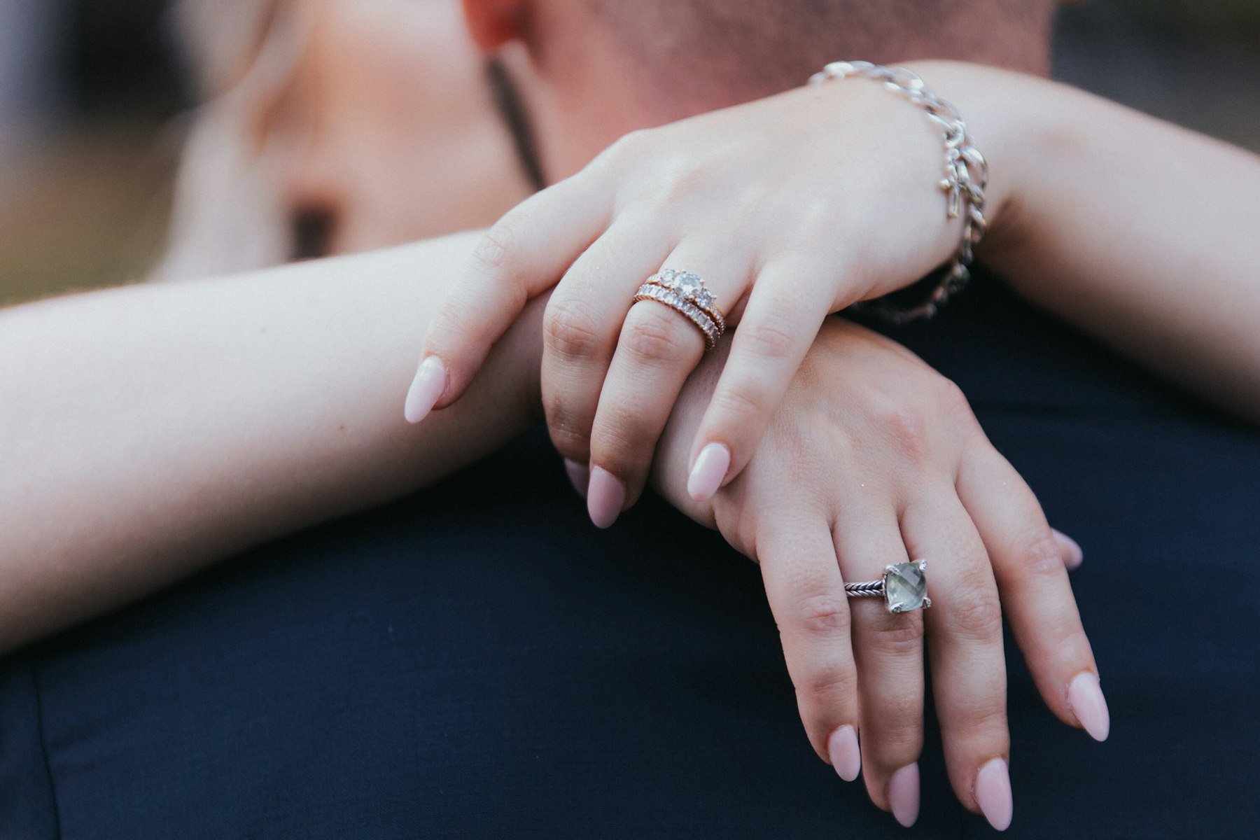 Bride's hands with rings and bracelet resting on the groom's arm at a white barn wedding