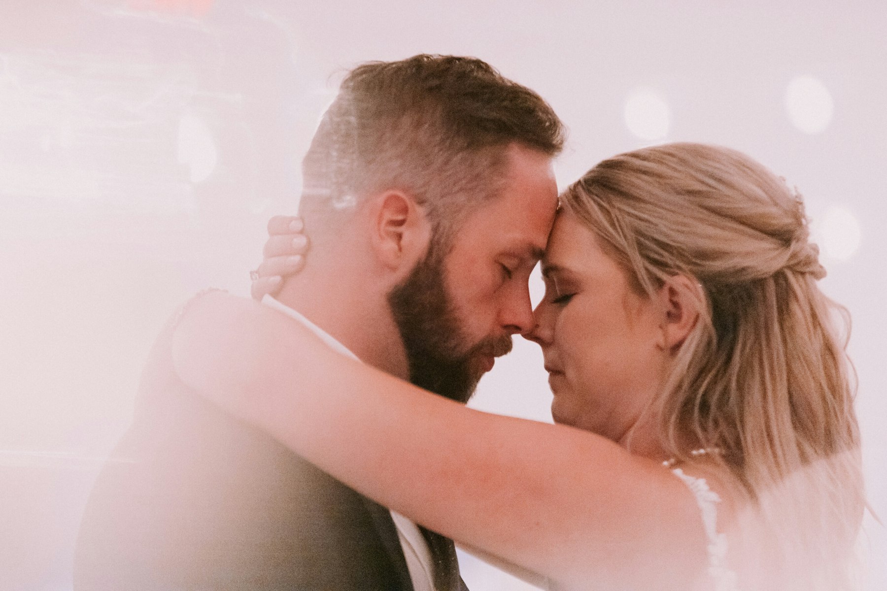Bride and groom forehead to forehead under string lights at a white barn wedding