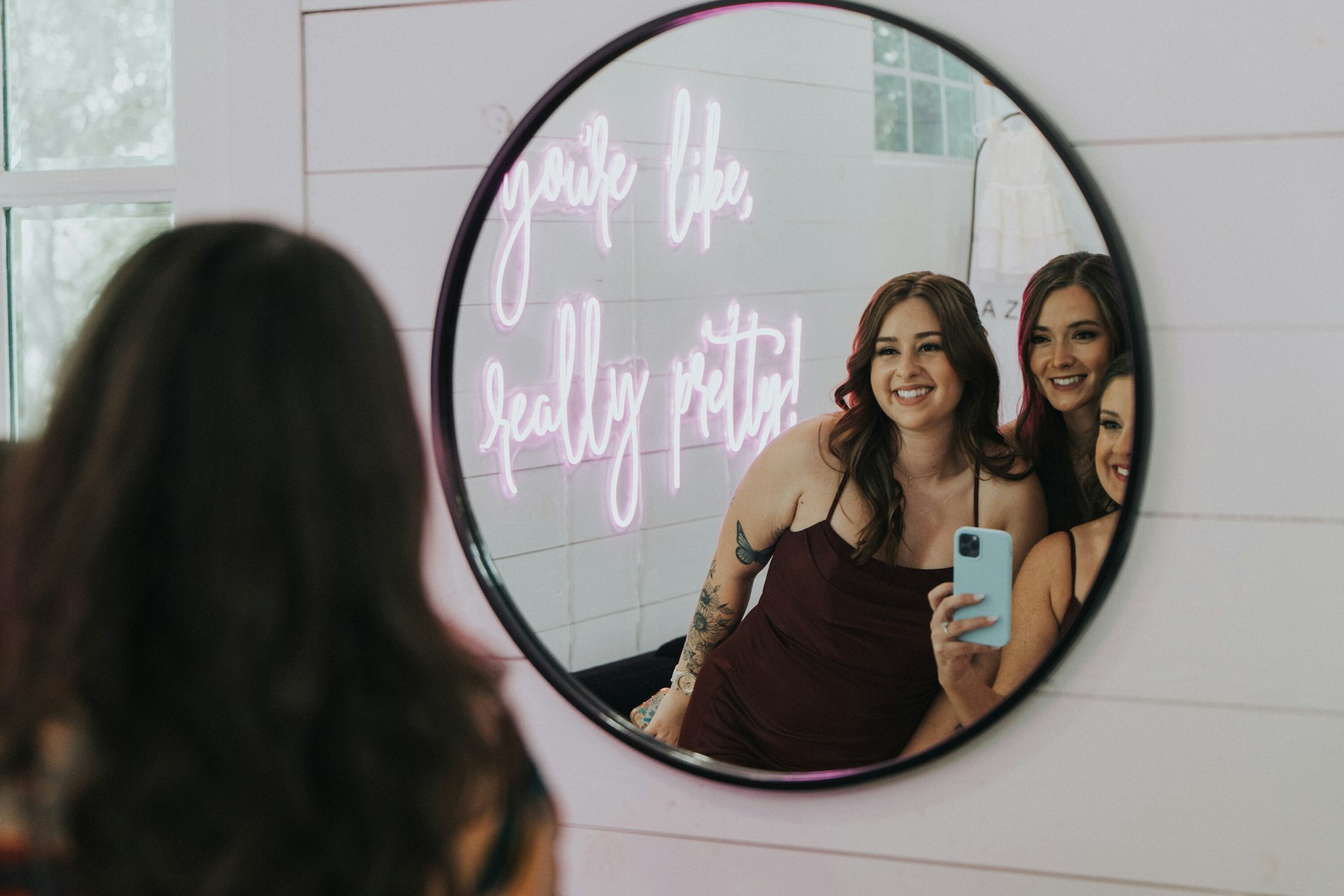 Bridesmaids reflected in a round mirror at a white barn wedding
