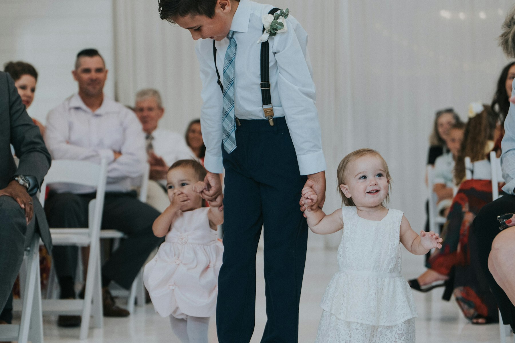 Flower girls walking down the aisle with a groomsman at a white barn wedding
